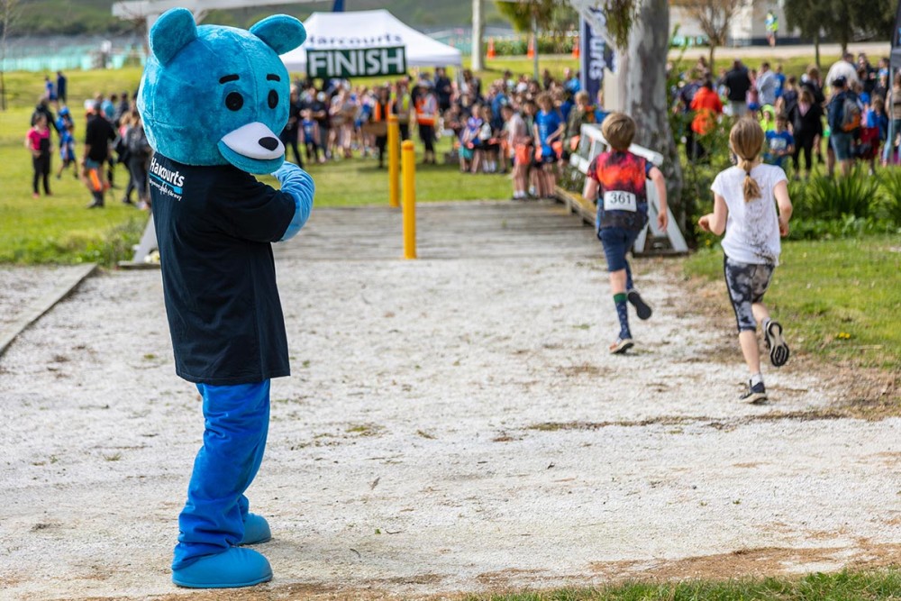 A large human sized blue teddy bear points towards the Kids duathlon finish line